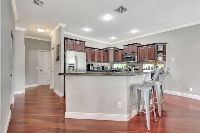 kitchen featuring a kitchen bar, backsplash, dark brown cabinetry, stainless steel appliances, and crown molding