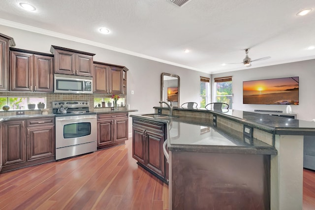 kitchen featuring ceiling fan, sink, dark hardwood / wood-style floors, an island with sink, and appliances with stainless steel finishes