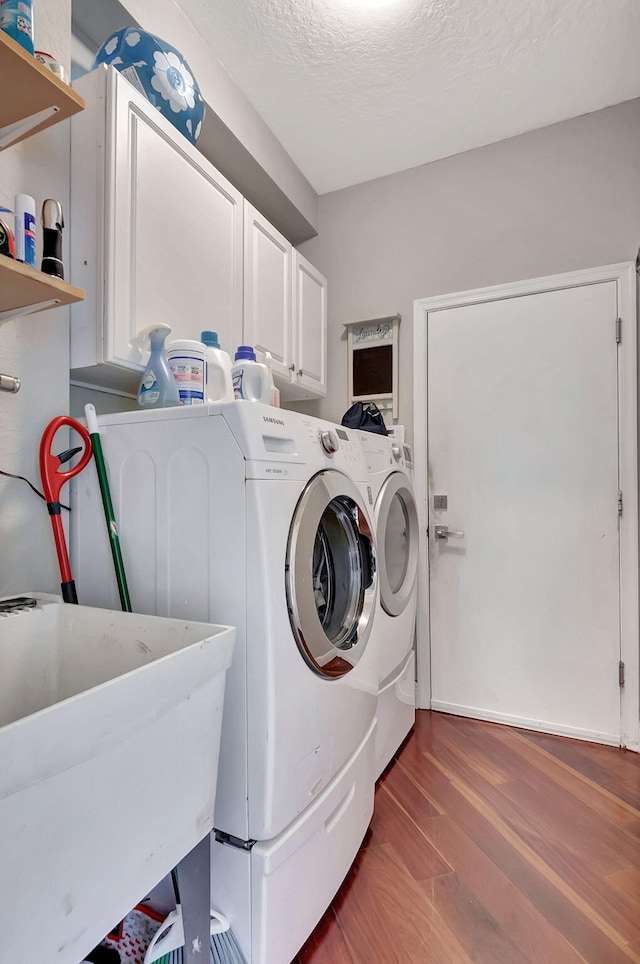 clothes washing area featuring cabinets, dark hardwood / wood-style flooring, a textured ceiling, sink, and washing machine and clothes dryer