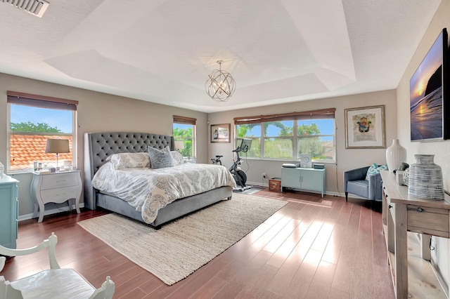 bedroom featuring a tray ceiling, dark wood-type flooring, and a notable chandelier