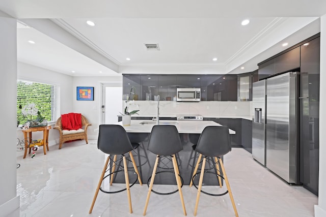 kitchen with a breakfast bar, a raised ceiling, stainless steel appliances, and an island with sink