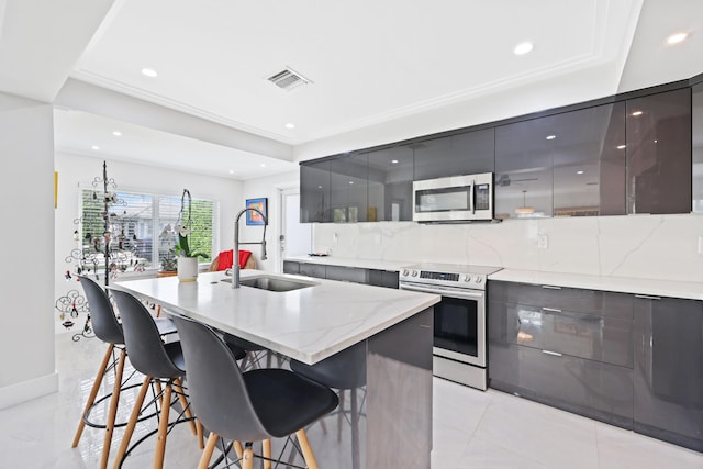 kitchen with decorative backsplash, a kitchen island with sink, sink, and appliances with stainless steel finishes