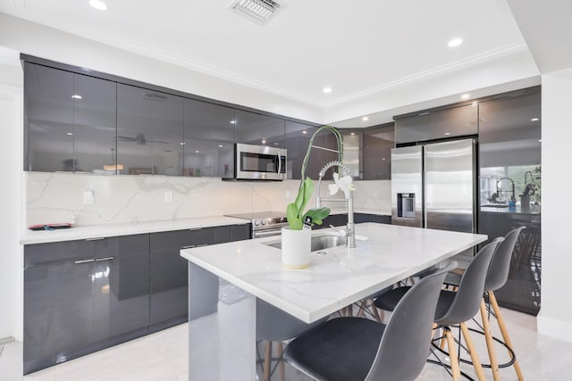 kitchen featuring a kitchen bar, backsplash, an island with sink, light stone counters, and stainless steel appliances