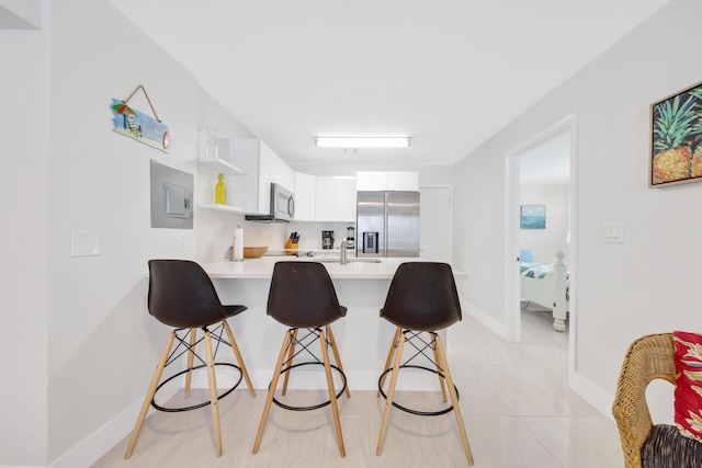 kitchen featuring a kitchen bar, kitchen peninsula, stainless steel appliances, light tile patterned floors, and white cabinets