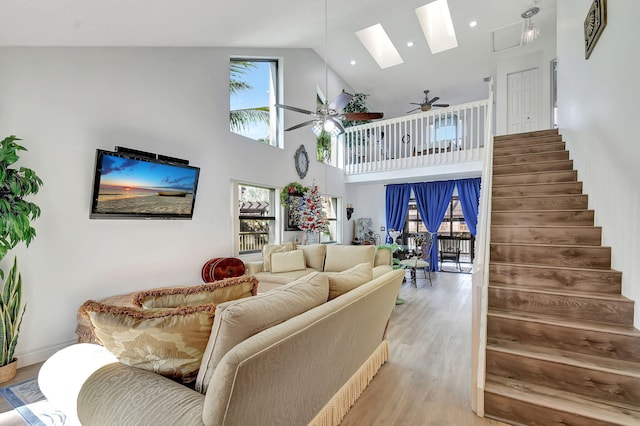 living room with a skylight, ceiling fan, high vaulted ceiling, and light hardwood / wood-style floors