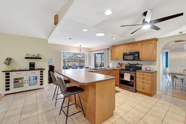 kitchen with ceiling fan, light tile patterned floors, decorative light fixtures, range with two ovens, and a breakfast bar area