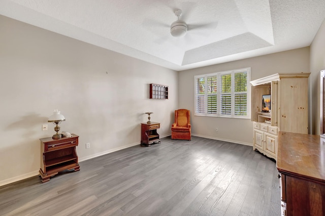 sitting room with ceiling fan, light hardwood / wood-style floors, a raised ceiling, and a textured ceiling