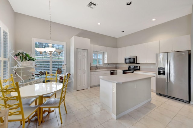 kitchen with stainless steel appliances, sink, white cabinets, a center island, and hanging light fixtures