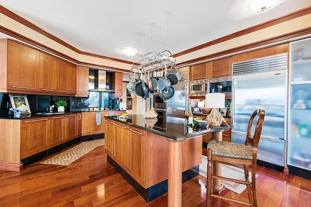 kitchen with built in appliances, a kitchen island, ornamental molding, and wall chimney range hood