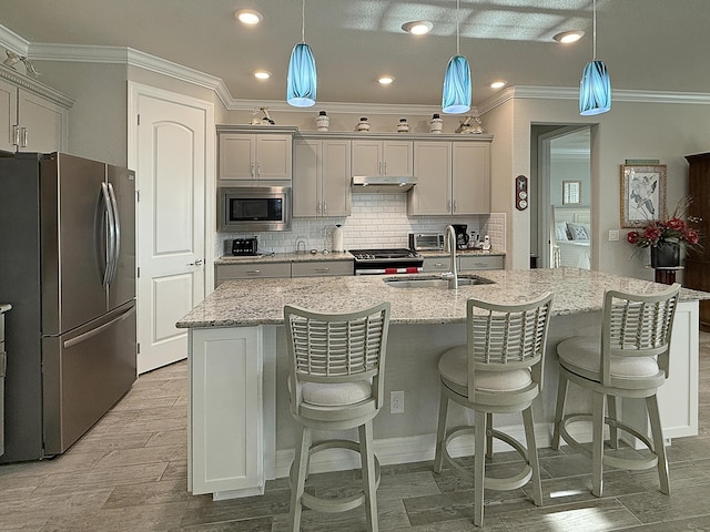 kitchen with appliances with stainless steel finishes, a kitchen island with sink, sink, and pendant lighting