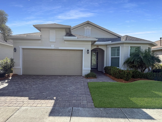12880 SW Aureolian Ln, Port Saint Lucie, FL 34987 - traditional home with a front lawn, a garage, a shingled roof, stucco siding, and decorative driveway