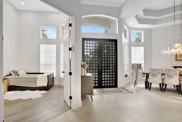 foyer entrance featuring an inviting chandelier, french doors, light hardwood / wood-style flooring, ornamental molding, and a towering ceiling