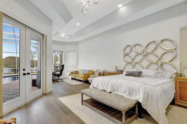 bedroom with french doors, access to outside, light hardwood / wood-style flooring, and a tray ceiling