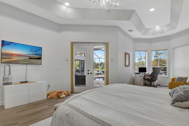 bedroom featuring access to exterior, french doors, light hardwood / wood-style floors, and a tray ceiling