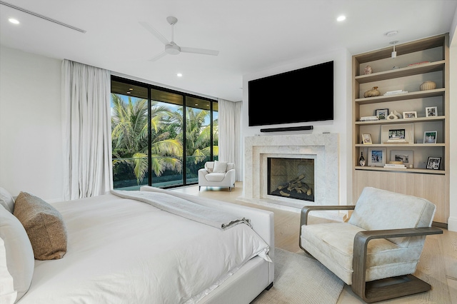 bedroom featuring floor to ceiling windows, access to exterior, ceiling fan, a premium fireplace, and light wood-type flooring