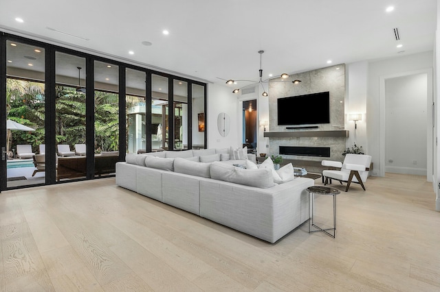 living room with light wood-type flooring, an inviting chandelier, a wall of windows, and a premium fireplace