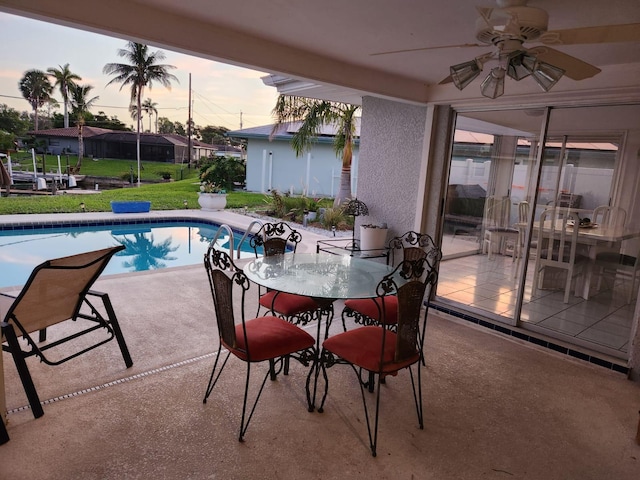 pool at dusk with a patio, ceiling fan, and a lawn