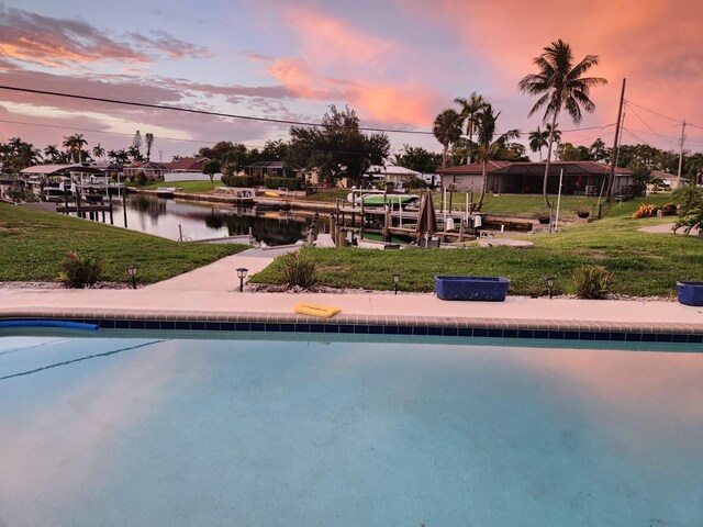 pool at dusk featuring a lawn, a boat dock, and a water view