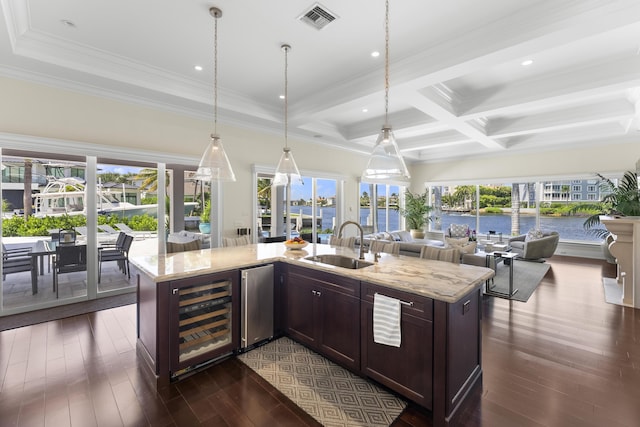 kitchen featuring a kitchen island with sink, sink, beverage cooler, and light stone counters