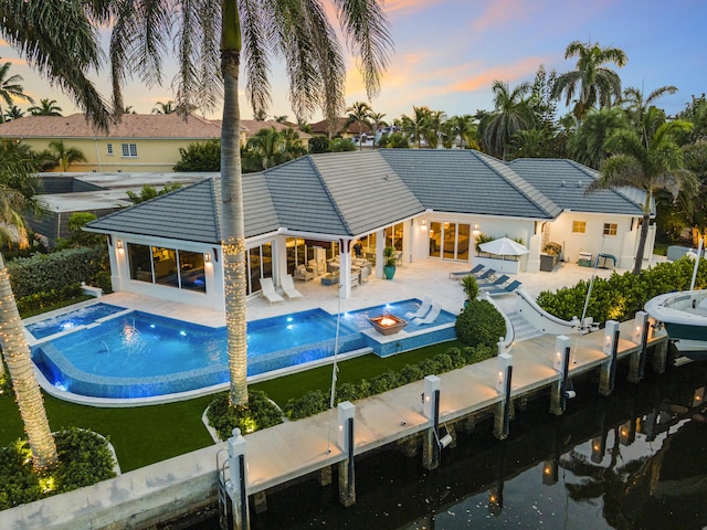 back house at dusk with a patio area and a pool with hot tub