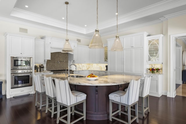 kitchen featuring a kitchen island with sink, white cabinets, appliances with stainless steel finishes, tasteful backsplash, and decorative light fixtures