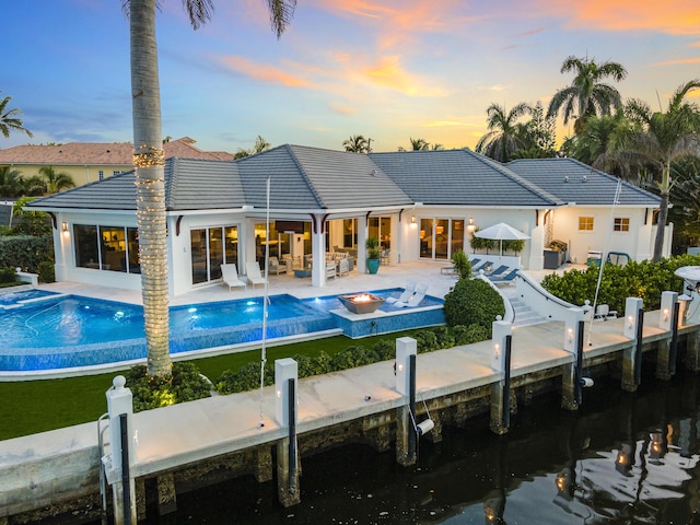 back house at dusk featuring pool water feature and a patio area