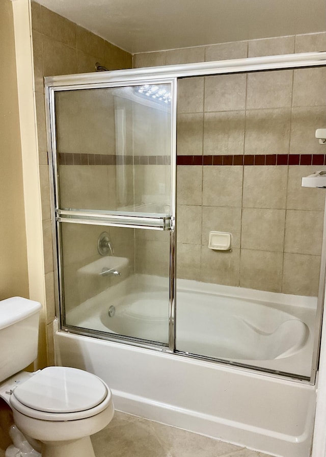 bathroom featuring tile patterned flooring, toilet, and bath / shower combo with glass door