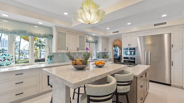 kitchen with a center island, crown molding, backsplash, appliances with stainless steel finishes, and glass insert cabinets