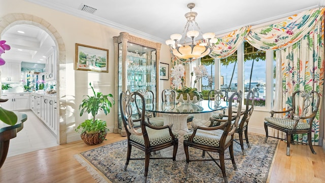 dining area with arched walkways, a notable chandelier, crown molding, visible vents, and light wood-type flooring