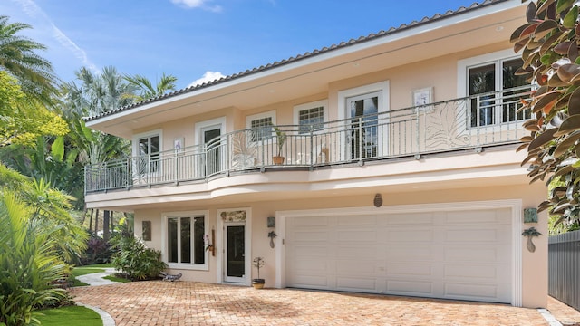 view of front of house featuring decorative driveway, a tile roof, stucco siding, a balcony, and a garage