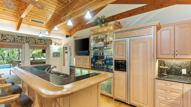 kitchen with vaulted ceiling with beams, a breakfast bar area, visible vents, a sink, and paneled built in refrigerator