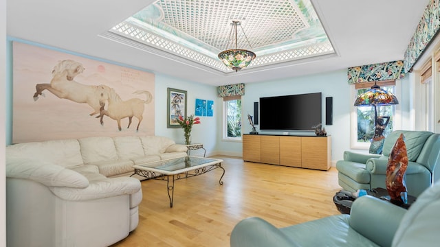 living area featuring a tray ceiling, baseboards, and light wood finished floors