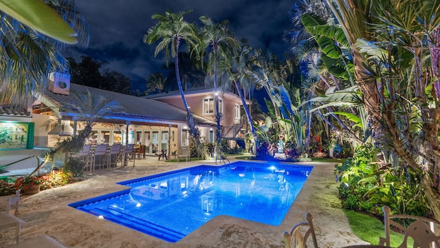 pool at twilight featuring a patio area, an outdoor pool, and outdoor dry bar