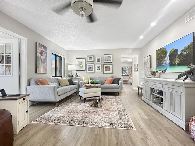 living room with ceiling fan, light hardwood / wood-style flooring, and a textured ceiling