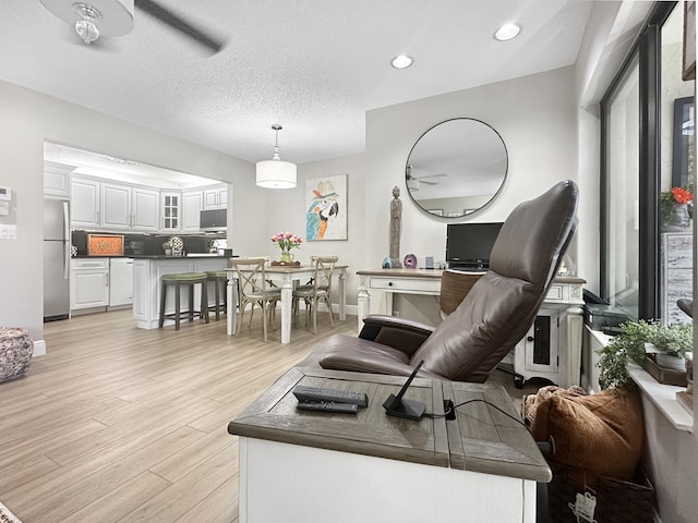 living room featuring ceiling fan, light hardwood / wood-style floors, and a textured ceiling