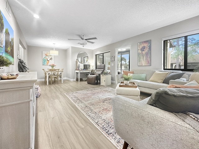 living room with a textured ceiling, light wood-type flooring, and ceiling fan