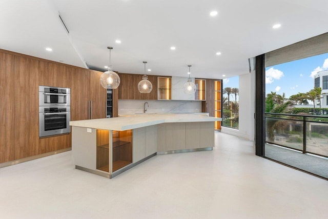 kitchen featuring sink, wood walls, stainless steel double oven, and hanging light fixtures