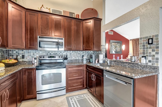 kitchen featuring backsplash, vaulted ceiling, dark stone countertops, light tile patterned floors, and stainless steel appliances