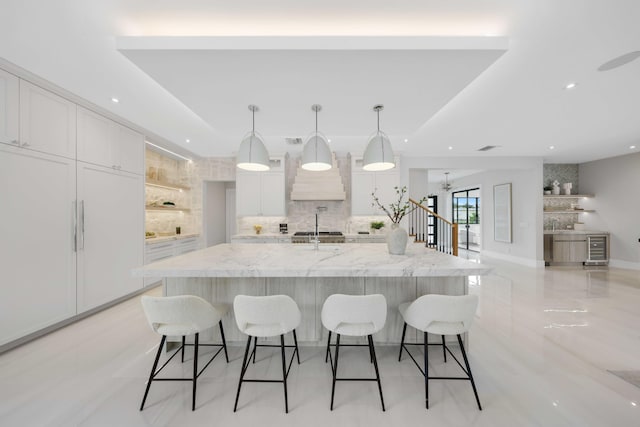 kitchen with pendant lighting, a large island with sink, white cabinets, tasteful backsplash, and light stone counters