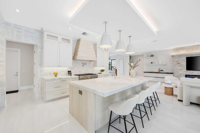 kitchen featuring premium range hood, white cabinetry, a kitchen island with sink, a kitchen breakfast bar, and hanging light fixtures