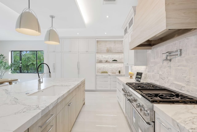 kitchen featuring premium range hood, pendant lighting, white cabinets, light stone counters, and sink