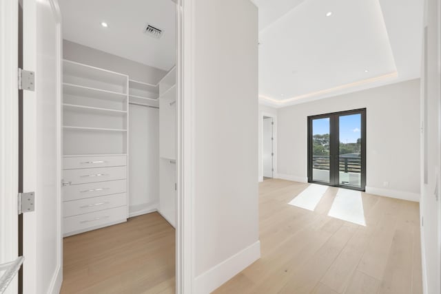 spacious closet with a raised ceiling, light hardwood / wood-style flooring, and french doors