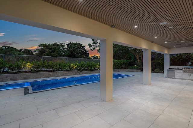 pool at dusk with area for grilling and a patio