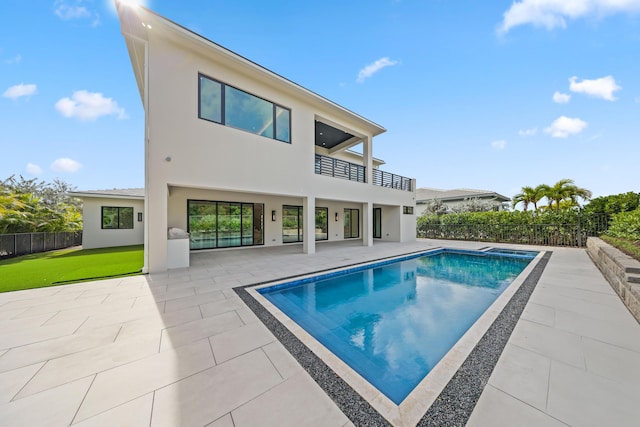 back of property featuring a fenced in pool, a patio area, a lawn, and a balcony