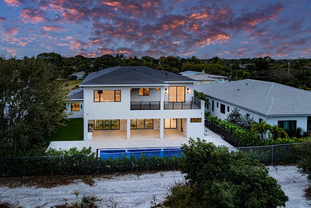 back house at dusk with a fenced in pool, a balcony, and a patio