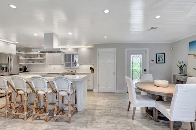 kitchen with island exhaust hood, white cabinetry, sink, and light wood-type flooring