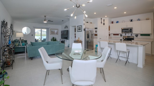 dining area featuring sink, ceiling fan with notable chandelier, vaulted ceiling, and light tile patterned flooring