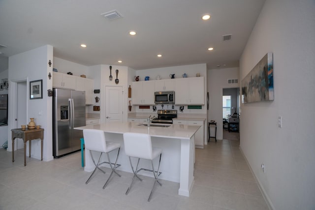 kitchen with a kitchen bar, stainless steel appliances, white cabinetry, and an island with sink