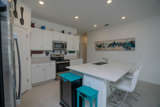 kitchen with a kitchen bar, appliances with stainless steel finishes, sink, a center island with sink, and white cabinetry