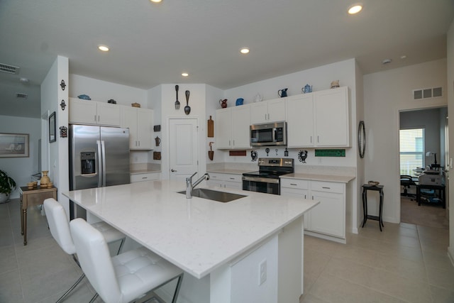 kitchen with sink, stainless steel appliances, an island with sink, a breakfast bar area, and white cabinets